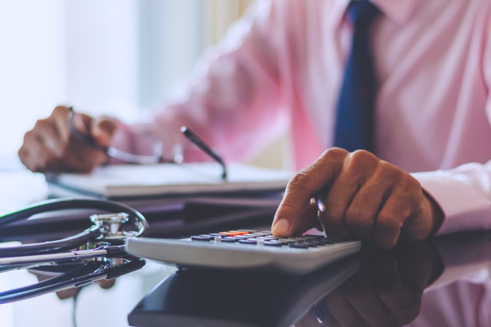 Male doctor works with finance using a calculator.